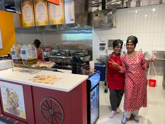 Two women smiling behind a red food cart at Madison Public Market